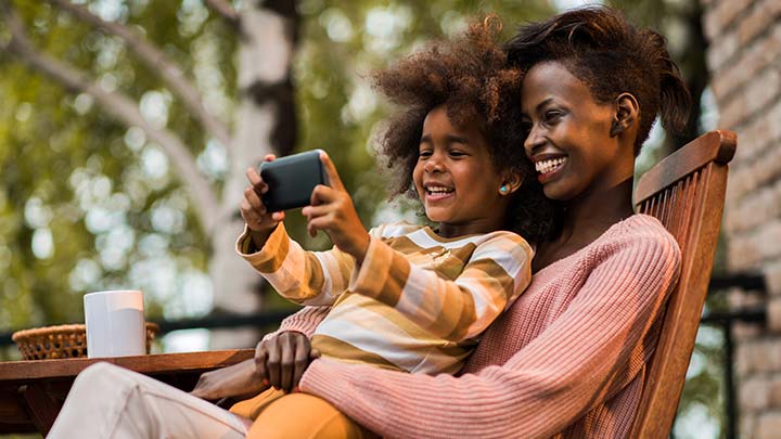 Mother and son sit outside in warm climate with a mobile phone on speaker, listening to Santa's Hotline