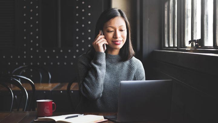 Wanita di telepon duduk di depan laptop